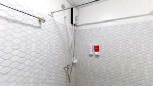 Ein Duschbereich mit strukturierter Wand, einer Handbrause und einer Bedienkonsole mit zwei Tasten.