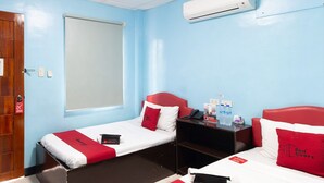 Ein Hotelzimmer mit zwei Einzelbetten, einem Fenster, einer Klimaanlage, einem Schreibtisch mit Stuhl und einem Nachttisch mit Lampe.