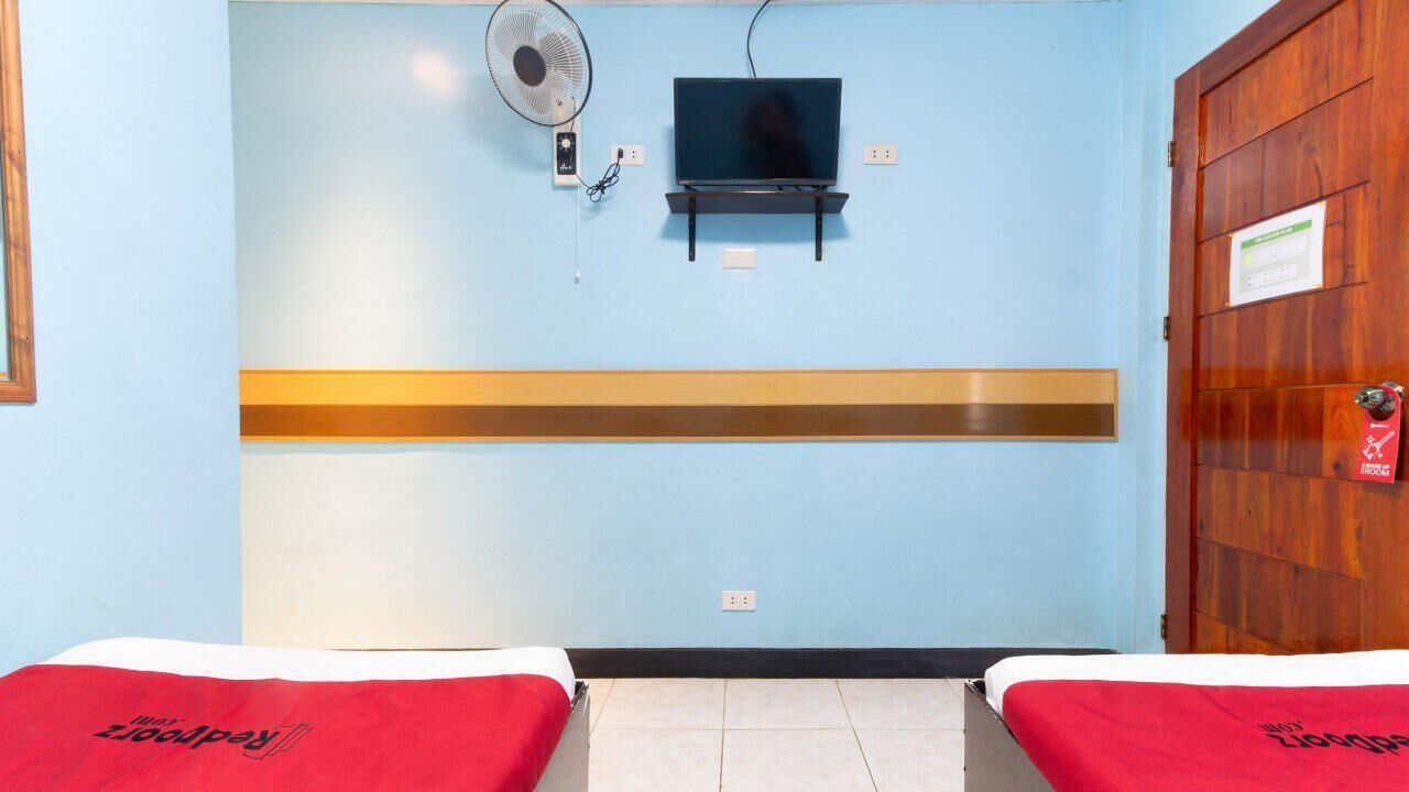 A room with a bed, a TV, a fan, and a wooden door.