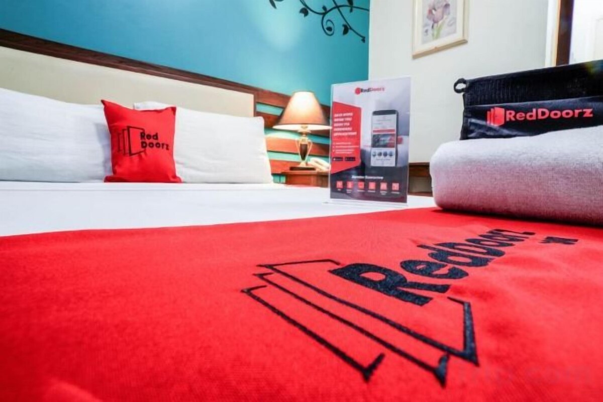Una habitación de hotel con cama, almohadas, una toalla de la marca RedDoorz y un letrero de RedDoorz en la pared.