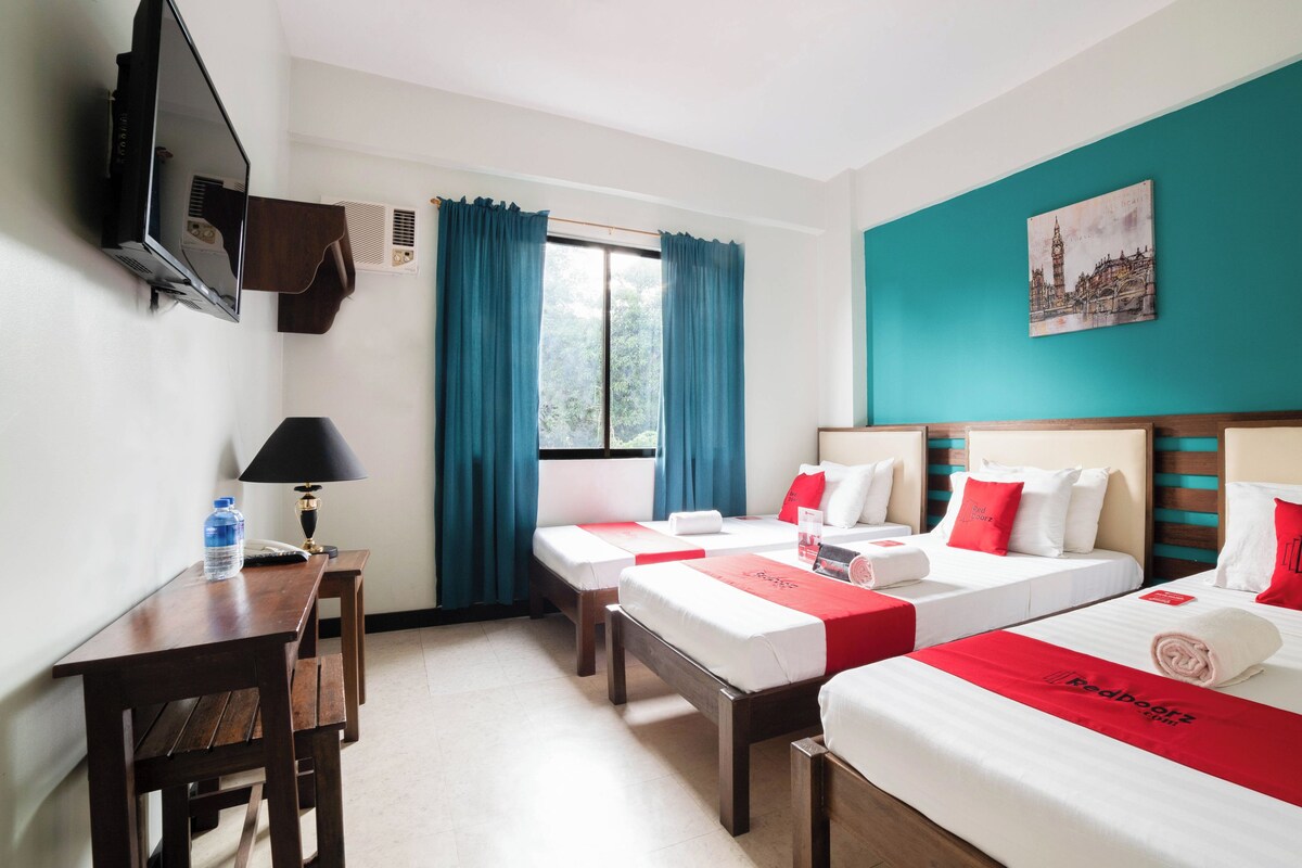 Habitación de hotel con dos camas, un escritorio, una silla, un televisor y una ventana con cortinas.