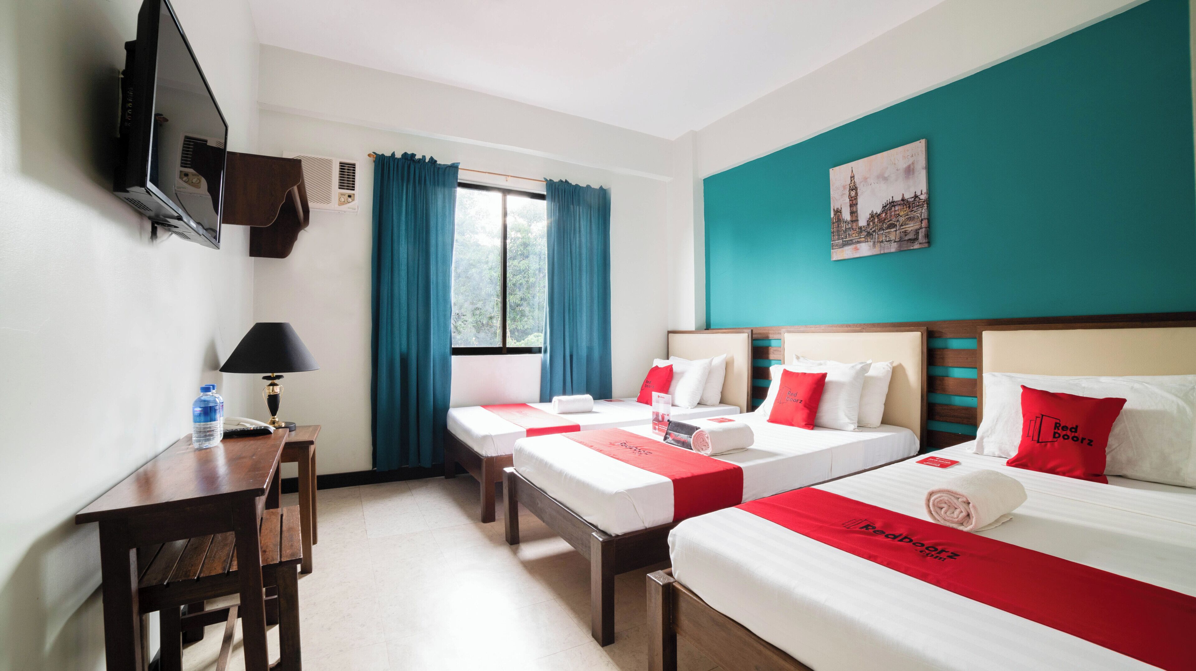 A hotel room with two beds, a desk, a chair, a TV, and a window with curtains.