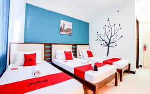 A hotel room with three beds, each with a red and white bedspread and pillows, a wall-mounted picture of a cityscape, and a tree decal.