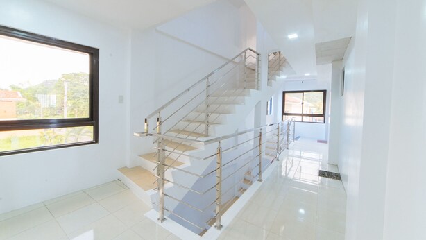 Un intérieur moderne avec un escalier, de grandes fenêtres et une palette de couleurs sobres, dominée par le blanc.