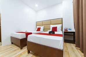 A hotel room with two beds, a wooden floor, a nightstand with a lamp, and a window with curtains. - RedDoorz Plus @ JNV Dream Hotel Subic Zambales (Subic)