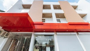 Un bâtiment moderne doté d’une façade rouge et blanche bien visible, de grandes fenêtres et d’un balcon apparent situé aux étages supérieurs.