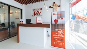 Un comptoir d’accueil avec une enseigne indiquant « Dream J&V Bed & Breakfast », une publicité pour l’application RedDoorz et une statue accrochée au mur.