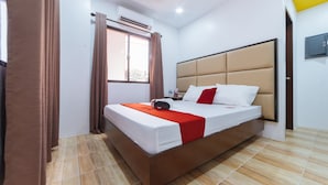 Une chambre d’hôtel avec un lit, une fenêtre avec des rideaux, un appareil de climatisation et une table de chevet.