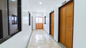 Un couloir propre et bien éclairé, avec un sol carrelé, des portes en bois et une fenêtre sur le côté gauche.