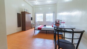 A room with a bed, a table with chairs, a wardrobe, and a window with curtains.