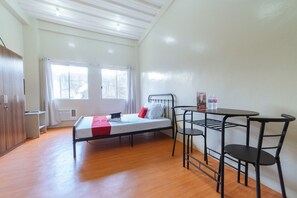 Une chambre de type dortoir, équipée d’un lit, d’un bureau, d’une chaise et d’une fenêtre.