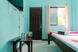 A room with a bed, a desk with a remote control, two water bottles, and a sign on the wall.