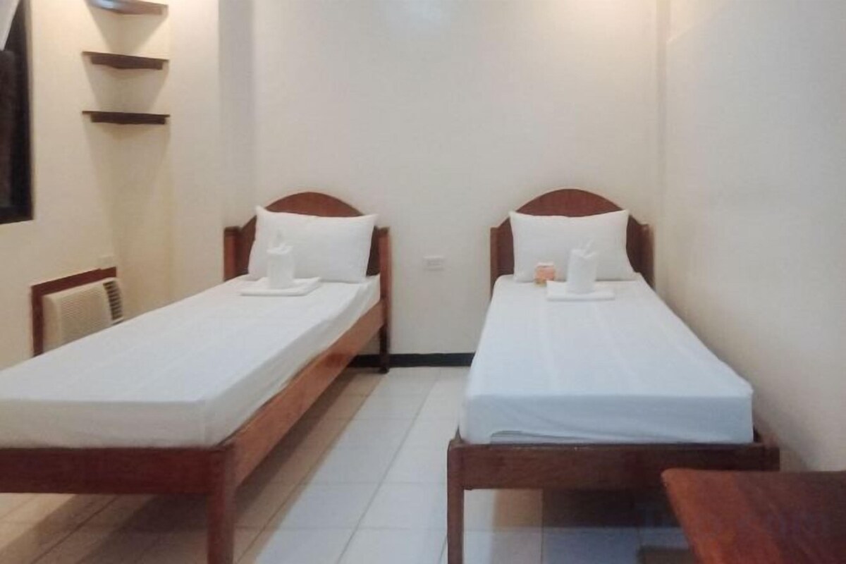 A room with two single beds, each with a wooden headboard and white bedding.