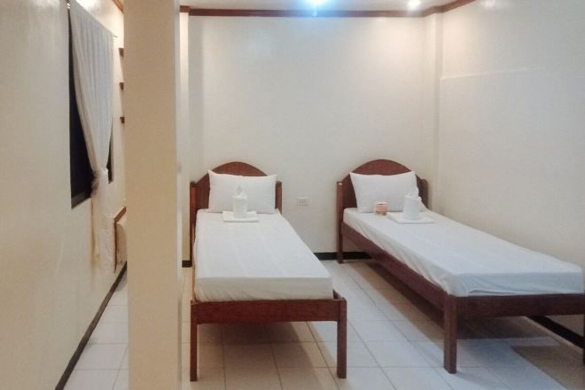 A small, clean room with two single beds, each with a pillow and a small table.
