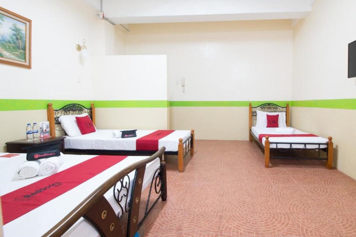 Quarto de hotel com duas camas de solteiro, uma escrivaninha com cadeira, televisão de tela plana na parede e uma faixa verde na parede.