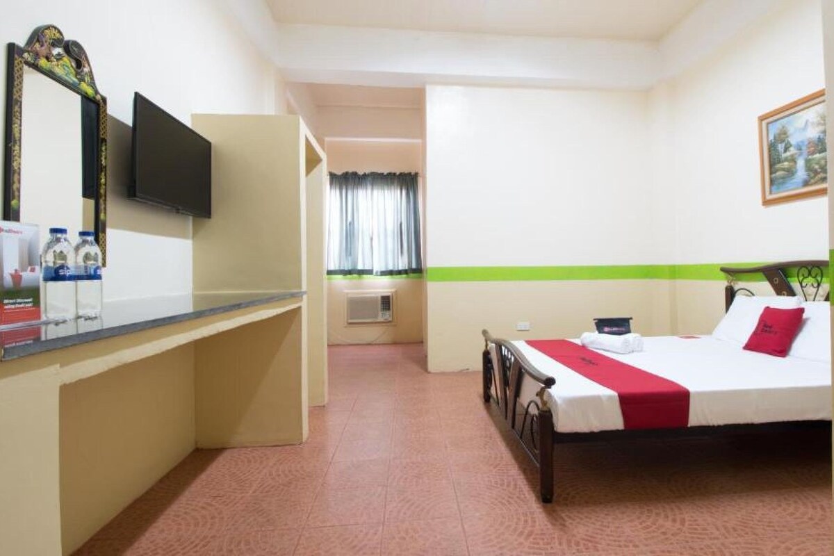 A hotel room with a bed, a desk with a mirror, a television, and a window with curtains.