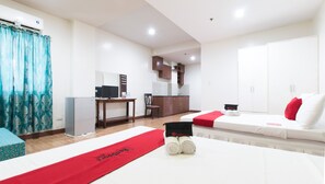 A hotel room with a bed, a desk with a computer, a chair, a wardrobe, and a kitchenette. - RedDoorz @ San Jose Tagbak Jaro Iloilo (Iloilo)