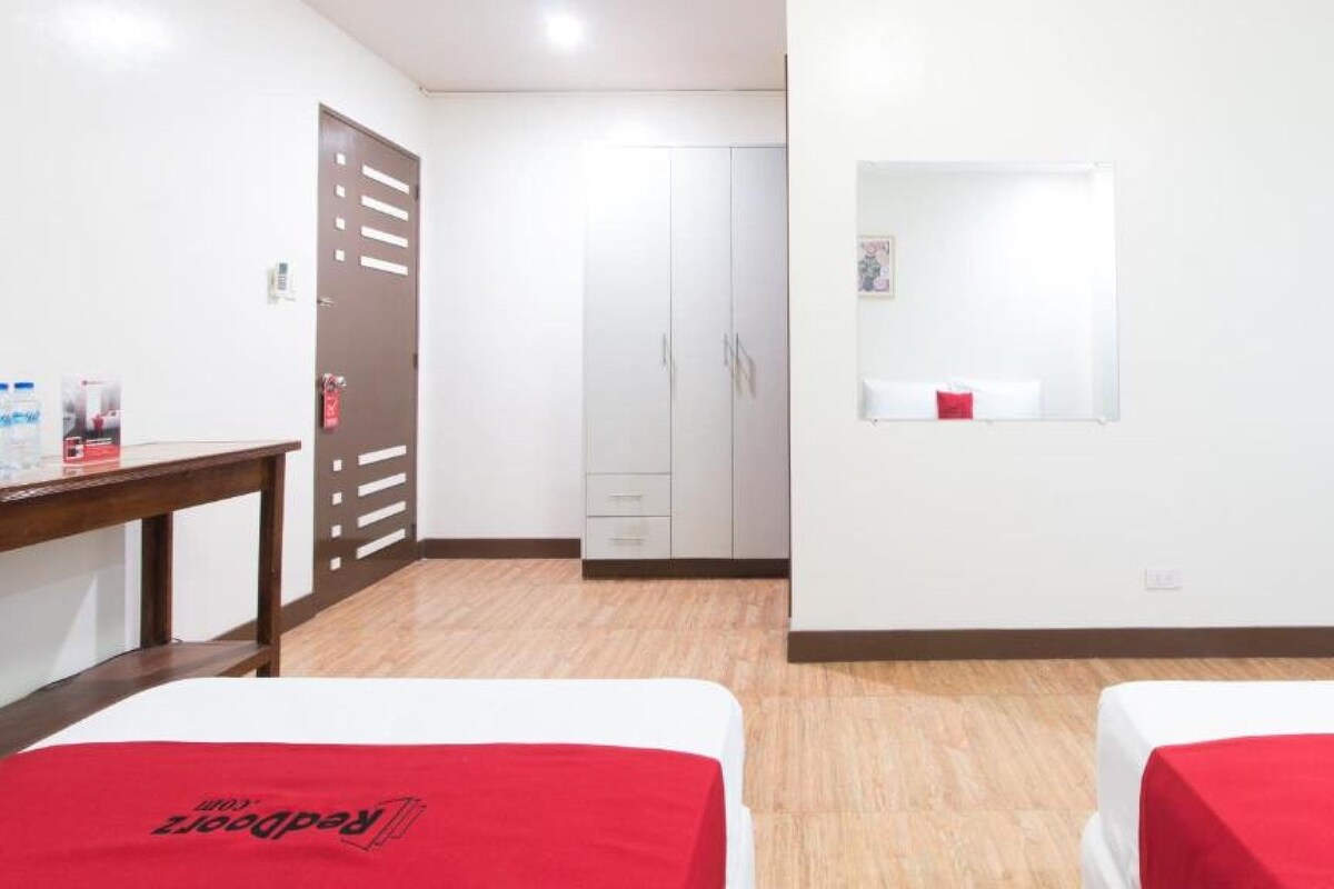Una habitación de hotel con dos camas, un escritorio de madera, un armario y un espejo en la pared.