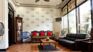 Uma sala de estar com sofá, mesa de centro, ventilador e parede decorada com logotipos repetidos.
