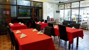 Restaurante com toalhas de mesa vermelhas, cadeiras pretas e uma grande janela com vista para o exterior.