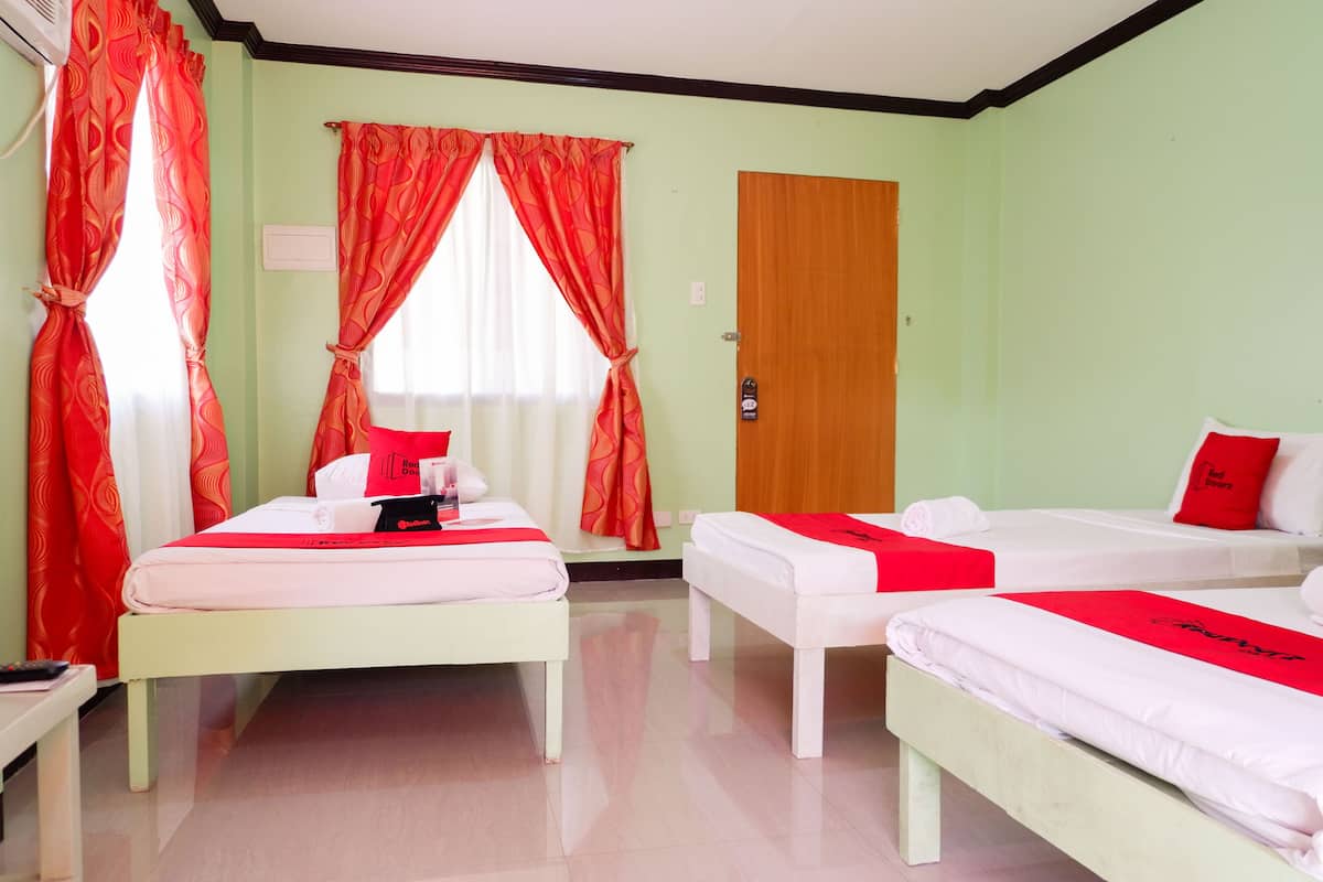 Ein Hotelzimmer mit zwei Betten, einer Holztür und roten Vorhängen.