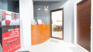 A hotel reception area with a RedDoorz sign, a wooden reception desk, a door leading to a dining area, and a large brown door. - RedDoorz near Liceo De Cagayan University Highschool (Cagayan de Oro)