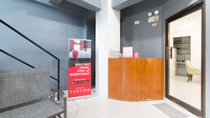 A reception area with a wooden desk, a red RedDoorz sign, a grey chair, and a staircase. - RedDoorz near Liceo De Cagayan University Highschool (Cagayan de Oro)