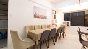 A dining area with a table set for six, surrounded by chairs, a cityscape painting, and a clock on the wall. - RedDoorz near Liceo De Cagayan University Highschool (Cagayan de Oro)