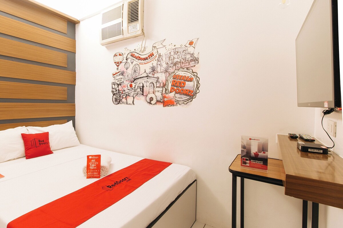 Ein Hotelzimmer mit einem Bett, dem Red Doors Logo auf dem Kopfkissen, einer Red Doors Reisebroschüre, einer Wanddekoration und einem Schreibtisch mit einem Red Doors Gerät.