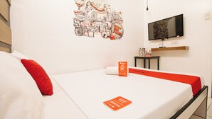 Une chambre d’hôtel avec un lit, un téléviseur fixé au mur et une petite table sur laquelle se trouvent une bouteille d’eau et une boîte.