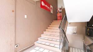 Un escalier orné d’une enseigne rouge RedDoorz, avec une rampe métallique et un mur de couleur beige.