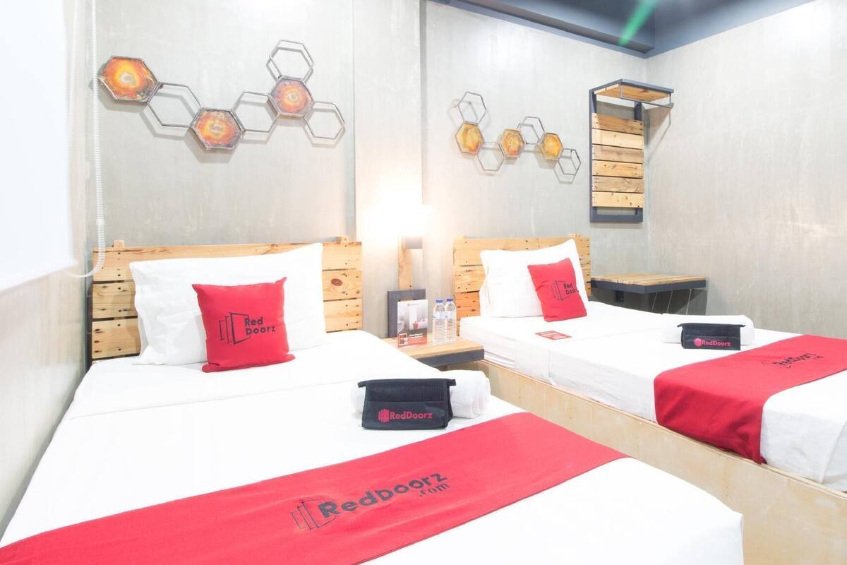 Dos camas con cabeceros de madera, ropa de cama blanca, almohadas rojas y el logotipo de RedDoorz.