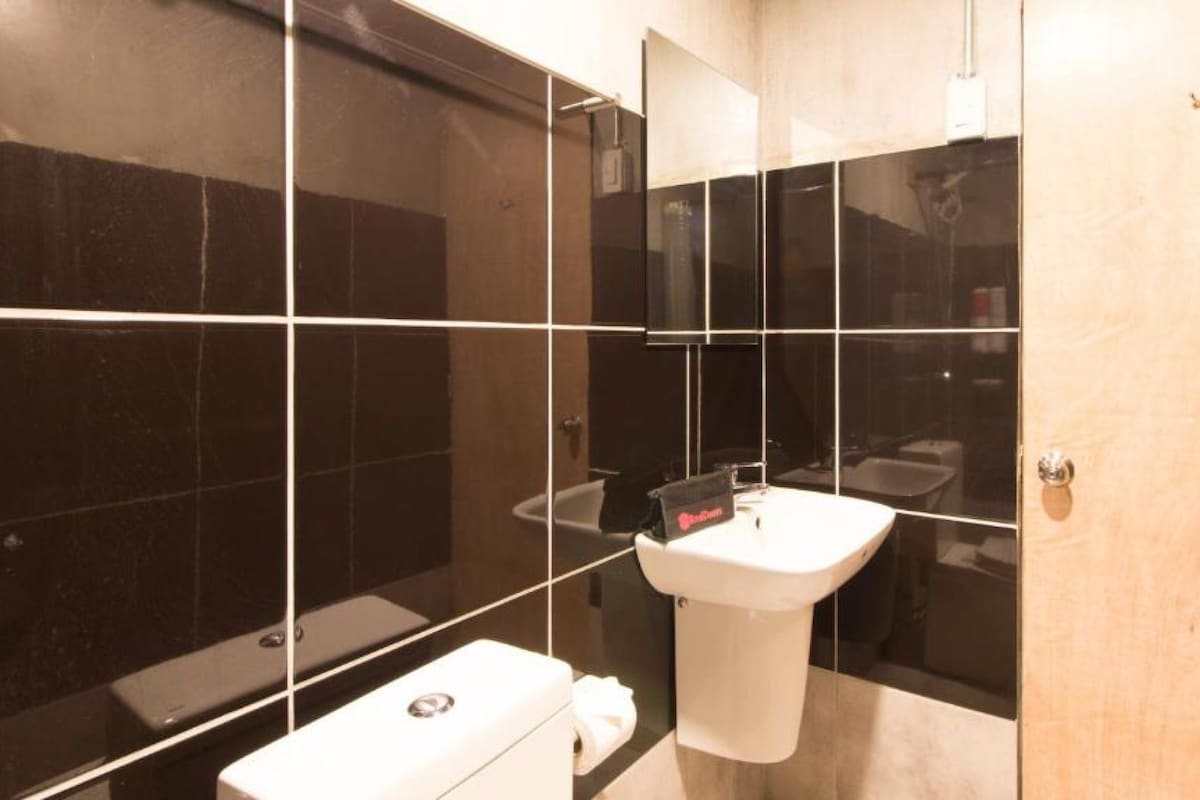 Ein modernes Badezimmer mit einem weißen Waschbecken, schwarzen Fliesenwänden und einer Duschkabine aus Glas.