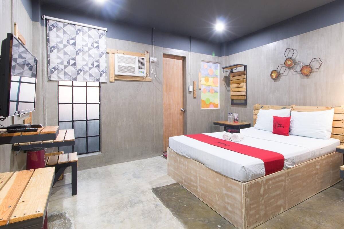 Un dormitorio con una cama de madera, un escritorio, una silla, un televisor y un ventanal con un diseño geométrico.