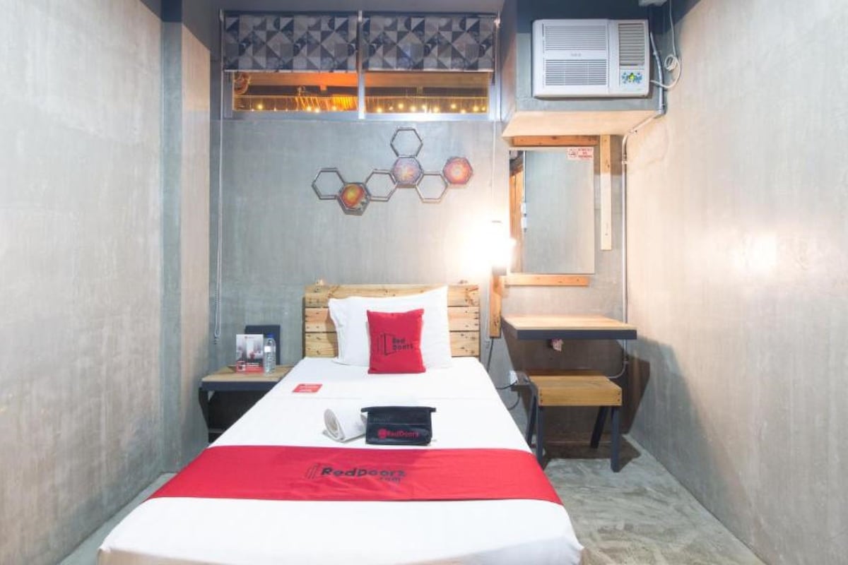 Ein kleines Hotelzimmer mit Bett, Nachttisch, Spiegel und Klimaanlage.