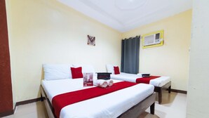 Habitación de hotel con dos camas, cada una con ropa blanca y detalles rojos, una mesita con mantel rojo y un equipo de aire acondicionado instalado en la pared.