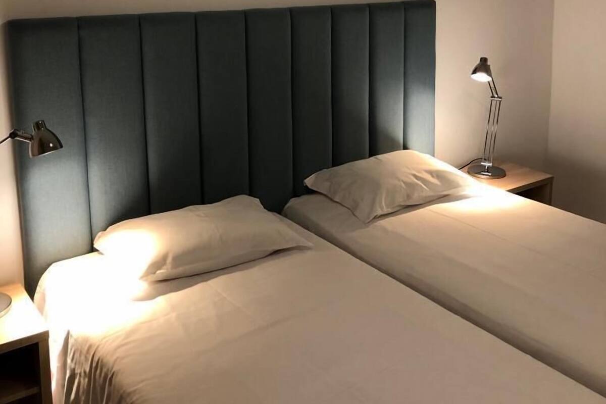 Ein Doppelbett mit gepolstertem Kopfteil, zwei Nachttische und zwei Lampen.