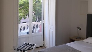 A bedroom with a bed, a nightstand, a lamp, a window with a view of greenery, and a drying rack. - Be Lisbon Residence Marquês (Lisbon)