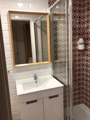 A bathroom with a white sink, a mirror with a wooden frame, and a shower with patterned tiles. - Be Lisbon Residence Marquês (Lisbon)