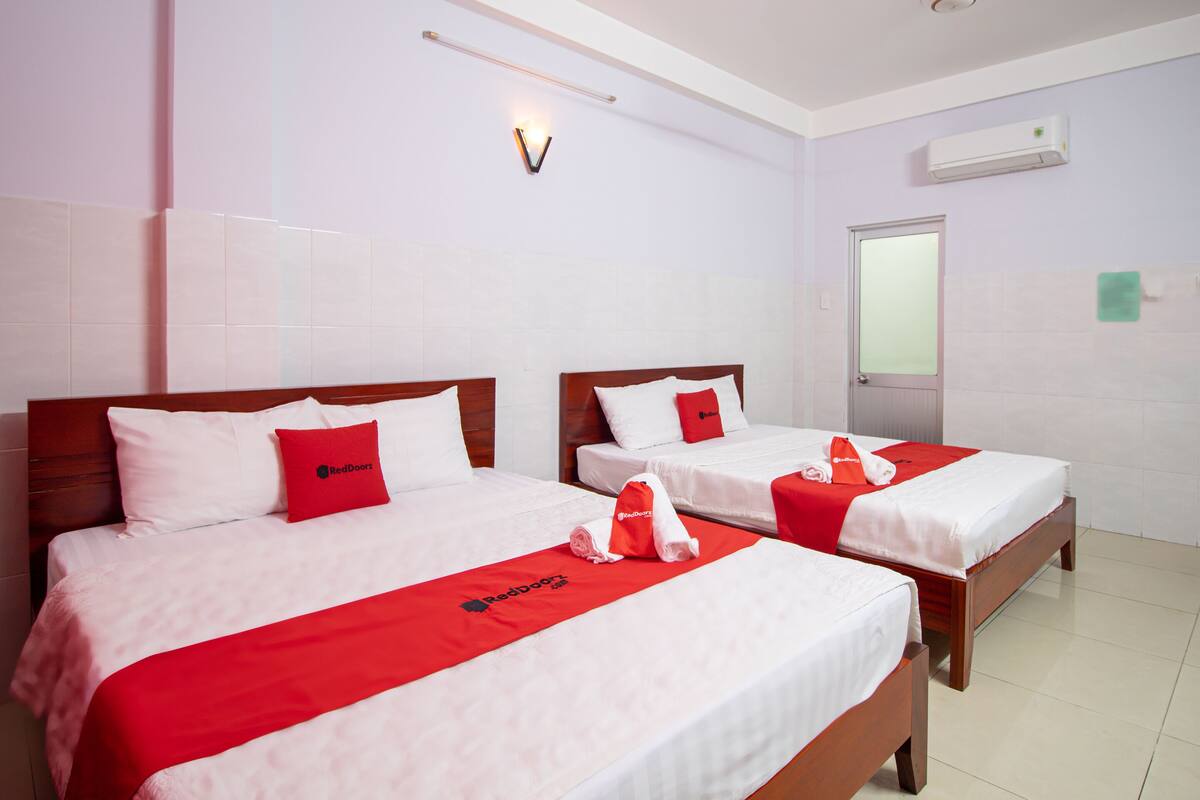 A hotel room with two beds, each with a red and white bedspread, a red pillow, and a towel with a logo.
