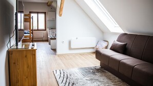Un espacio tipo loft con techo inclinado, un escritorio de madera, un sofá marrón y vistas a través de un tragaluz.
