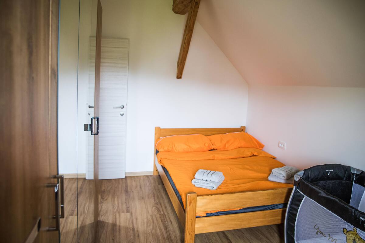 A bedroom with a wooden bed, an orange bedspread, a white door, and a small tent-like structure.