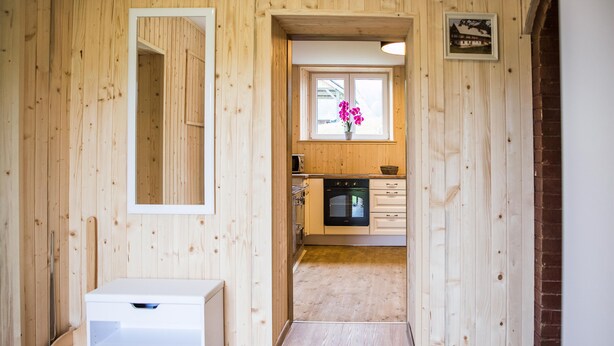 Un interior de madera con una zona de cocina, un armario blanco y una ventana con flores.