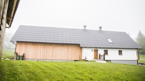 Una casa de dos pisos con un granero de madera adosado, un techo inclinado y un pequeño porche.
