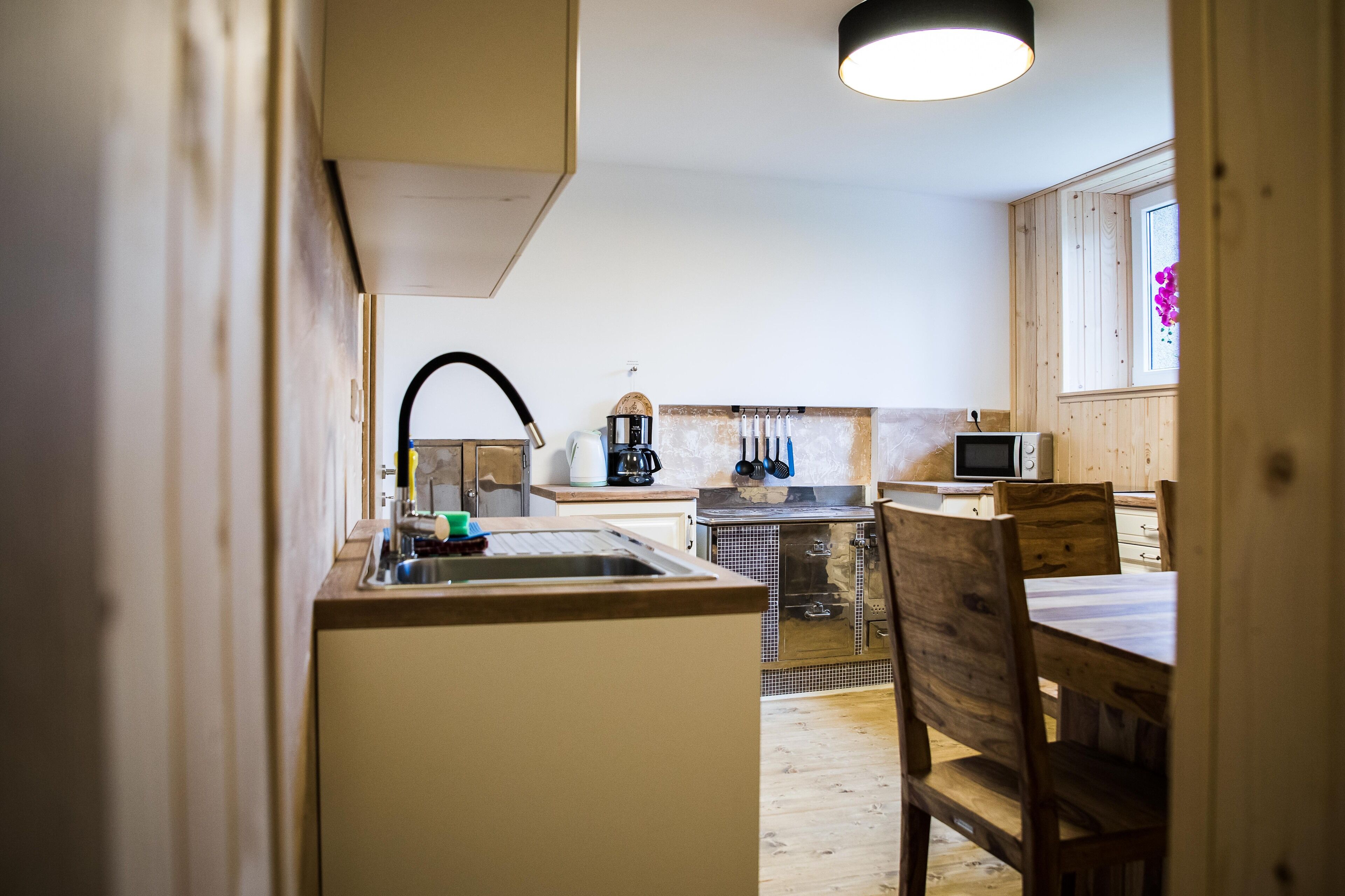 Een kleine keuken met een spoelbak, een magnetron en een koffiezetapparaat. Er is een houten tafel met stoelen.