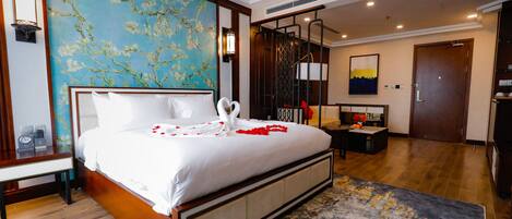 Habitación de hotel con una cama grande, cabecera de madera, un mural floral azul en la pared, un escritorio moderno y una puerta que da a otra habitación.