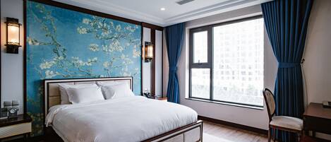 Habitación de hotel moderna con una cama grande, un escritorio y una silla. Se ve una ventana con cortinas y vistas a la ciudad.