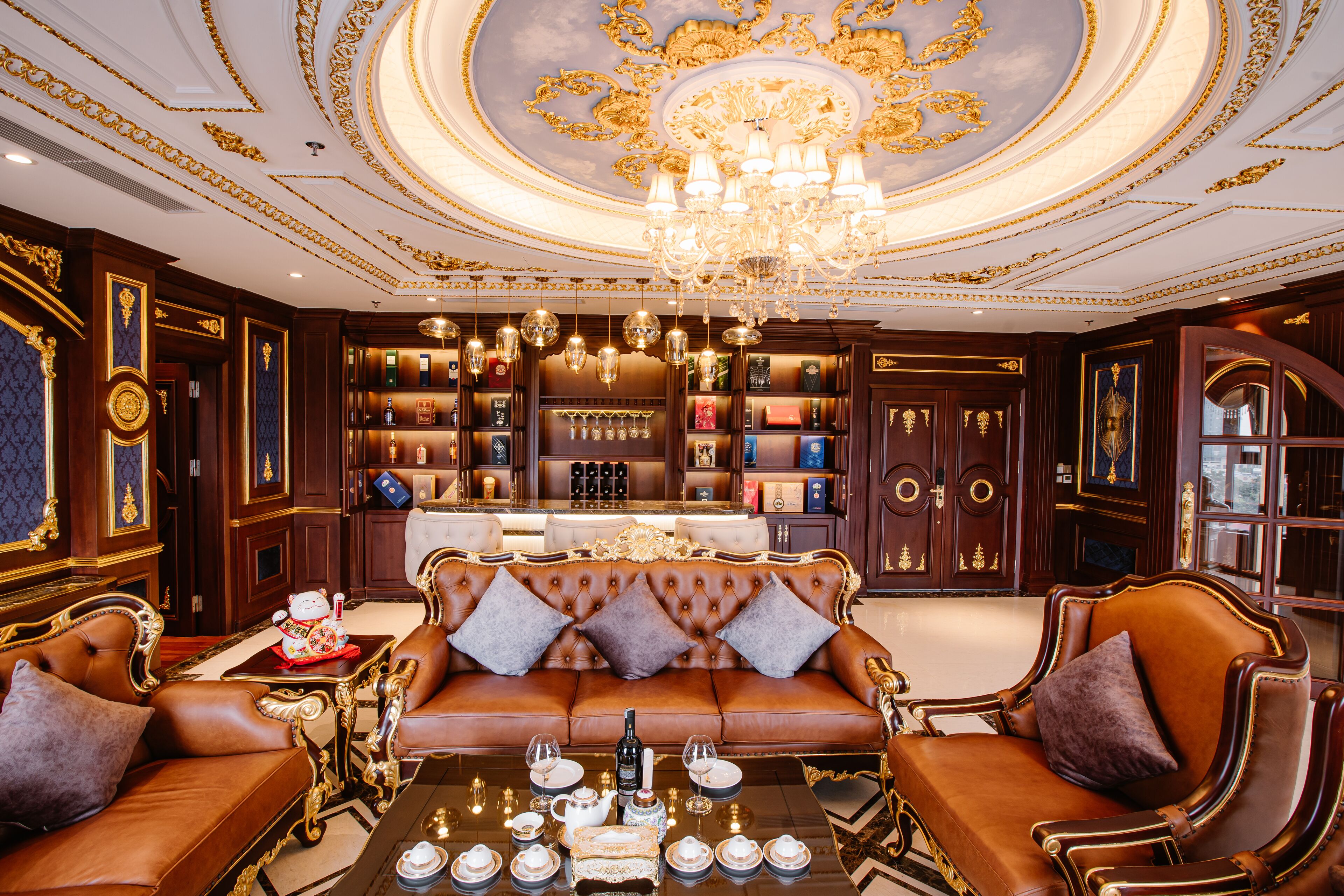 A luxurious room with a brown leather sofa, a chandelier, and a bar area with shelves of bottles.