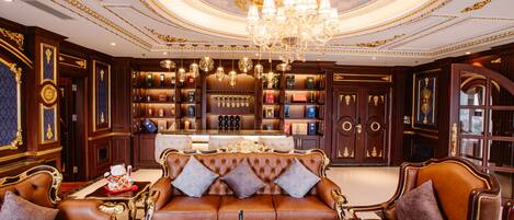 A luxurious room with a brown leather sofa, a chandelier, and a bar area with shelves of bottles.
