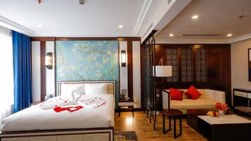 Quarto de hotel com uma cama grande, um sofá, uma mesa de centro e uma parede decorativa com padrão floral.